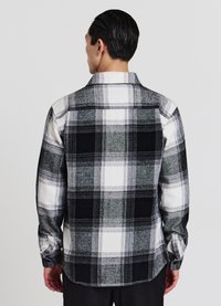 Chemise en flanelle à carreaux noirs, blancs et gris avec manches longues. Comprend un col boutonné et un ourlet incurvé. Tissu texturé et doux.