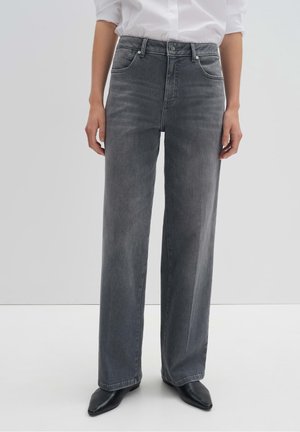Person iført mørkegrå jeans med høj talje og lige ben med lommer, kombineret med sorte spidse sko og en hvid skjorte.