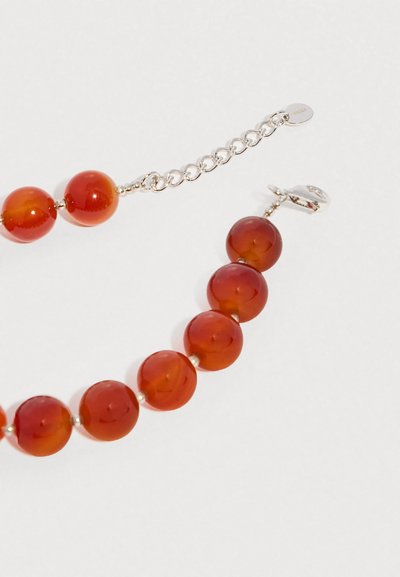 Βραχιόλι με στρογγυλές, γυαλισμένες χάντρες κεχριμπαριού και ασημένια αλυσίδα επέκτασης με κούμπωμα σε ανοιχτό φόντο.