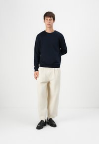 Sweat-shirt bleu marine à col rond, associé à un pantalon crème ample et des mocassins noirs. Textures lisses, design minimaliste.