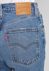 Vue arrière d’un jean Levi's bleu montrant la poche arrière avec surpiqûres et l’étiquette en cuir de la marque à la taille.