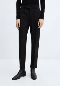 Zwarte pantalon met een getailleerde pasvorm, voorzien van een vlakke voorkant, riemlussen en zijzakken, in combinatie met zwarte leren enkellaarsjes.