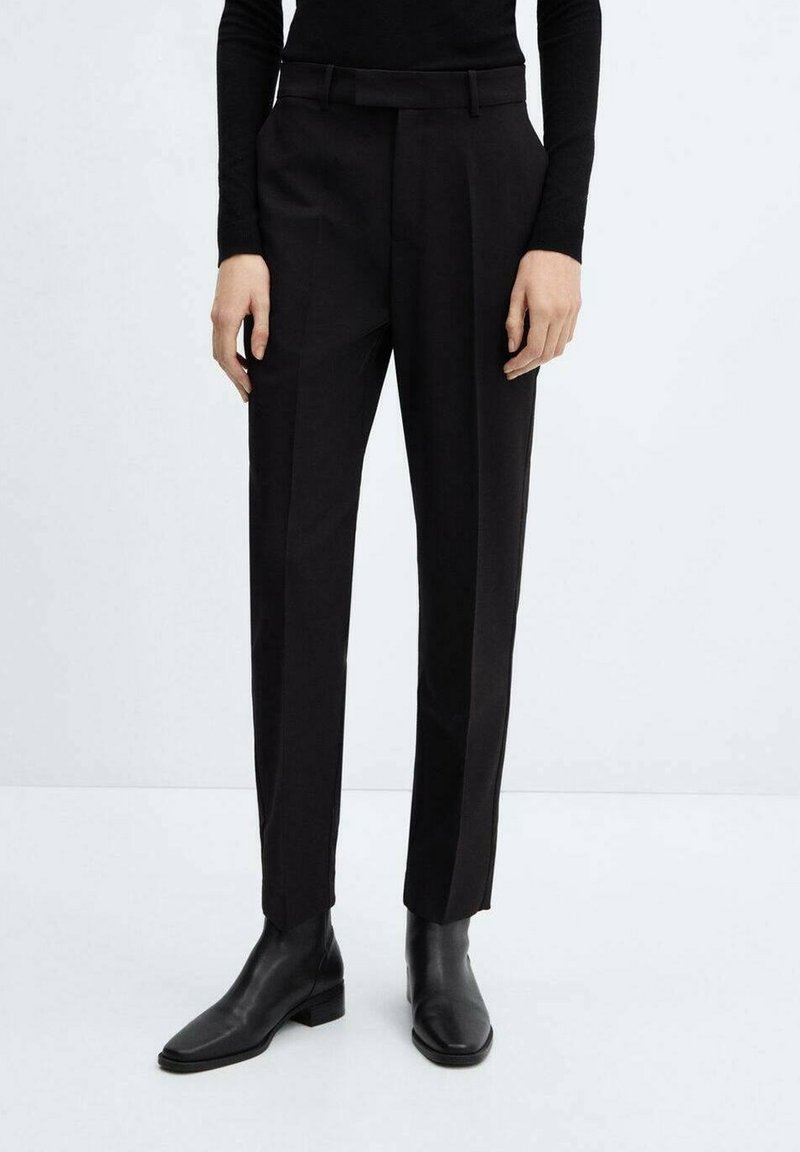 Zwarte pantalon met een getailleerde pasvorm, voorzien van een vlakke voorkant, riemlussen en zijzakken, in combinatie met zwarte leren enkellaarsjes.