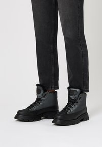 Botas de senderismo negras con un upper impermeable, cierre de cordones y ribete de pelo en el cuello. Suela de goma gruesa con dibujo texturizado para tracción.