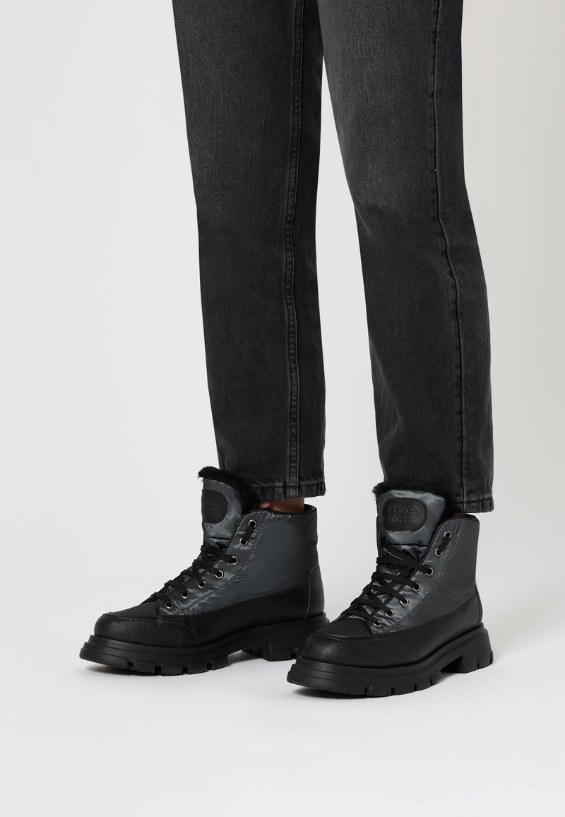 Botas de senderismo negras con un upper impermeable, cierre de cordones y ribete de pelo en el cuello. Suela de goma gruesa con dibujo texturizado para tracción.