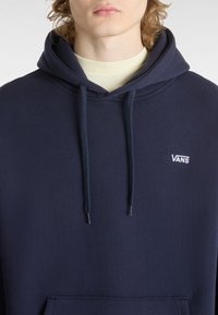 Felpa blu navy realizzata in tessuto testurizzato, con tasca a kangaroo, cordoncini regolabili e logo bianco Vans sul petto.