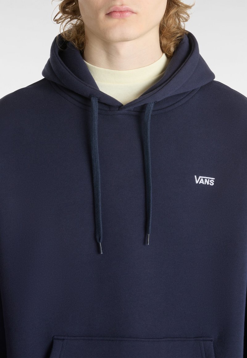 Granatowy hoodie wykonany z teksturowanej tkaniny, z kieszenią kangurką, regulowanymi sznurkami i białym logo Vans na klatce piersiowej.