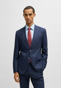 Navy blue suit with a textured pattern, single-button closure, notch lapels, paired with a light blue shirt and red patterned tie.
