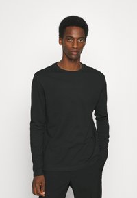 Svart langermet t-skjorte laget av myk stoff med rund hals, har en tettsittende form og minimalistisk design. Ingen mønstre eller aksenter.