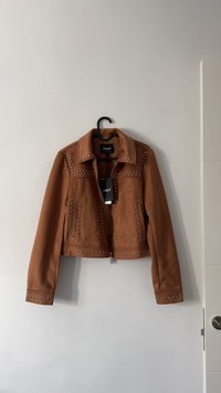 Giacca in suede color cammello dal design corto, dettagli con borchie sulle spalle e sull'orlo, chiusura con cerniera e etichetta brandizzata applicata.