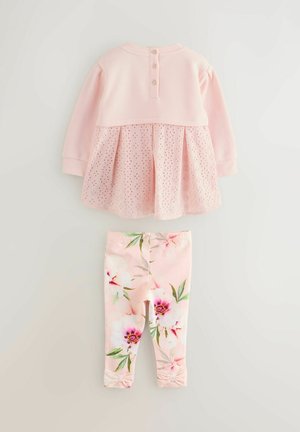 Vaaleanpunainen pitkähihainen paita, jossa on silmukkayksityiskohtia ja kolme nappia selässä, yhdistettynä kukkakuosisisiin leggingsseihin, joissa on nauhat nilkoissa.