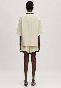 Kremfarbener Kurzarmtop mit schwarzem wellenförmigem Kragen, kombiniert mit passenden Shorts mit gewelltem Saum. Glatte Textur, lässige Passform.