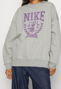 Grå sweatshirt i bomullsblandning, med en stor lila Nike-logga, skölddesign och texten 'Oregon 1972'. Avslappnad passform med ribbade ärmslut.