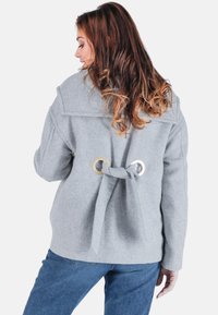 Graue Wolljacke mit großem Kragen, runder goldener Hardware und einer Bindung auf der Rückseite. Texturiert und mit lockerer Passform.