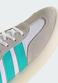 Jasnoszary zamszowy trampek z białymi panelami z tkaniny, turkusowymi paskami i białymi sznurówkami. Podeszwa w kremowym kolorze o gładkim wykończeniu.