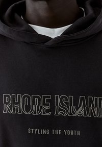 Czarna bluza z kapturem z miękkiego materiału z wyraźnym białym napisem "RHODE ISLAND" oraz mniejszym napisem "STYLING THE YOUTH" w kontrastowym wzorze.