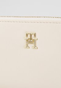 Portafoglio beige con zip realizzato in pelle liscia; presenta un accento del logo in tonalità oro stampato sul davanti. Dettaglio in tessuto testurizzato sulla zip superiore.
