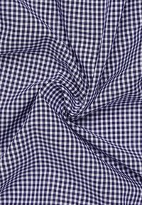 Tessuto in gingham blu navy e bianco con un motivo a scacchi, caratterizzato da una texture liscia e una leggera lucentezza, disposto in una forma attorcigliata.