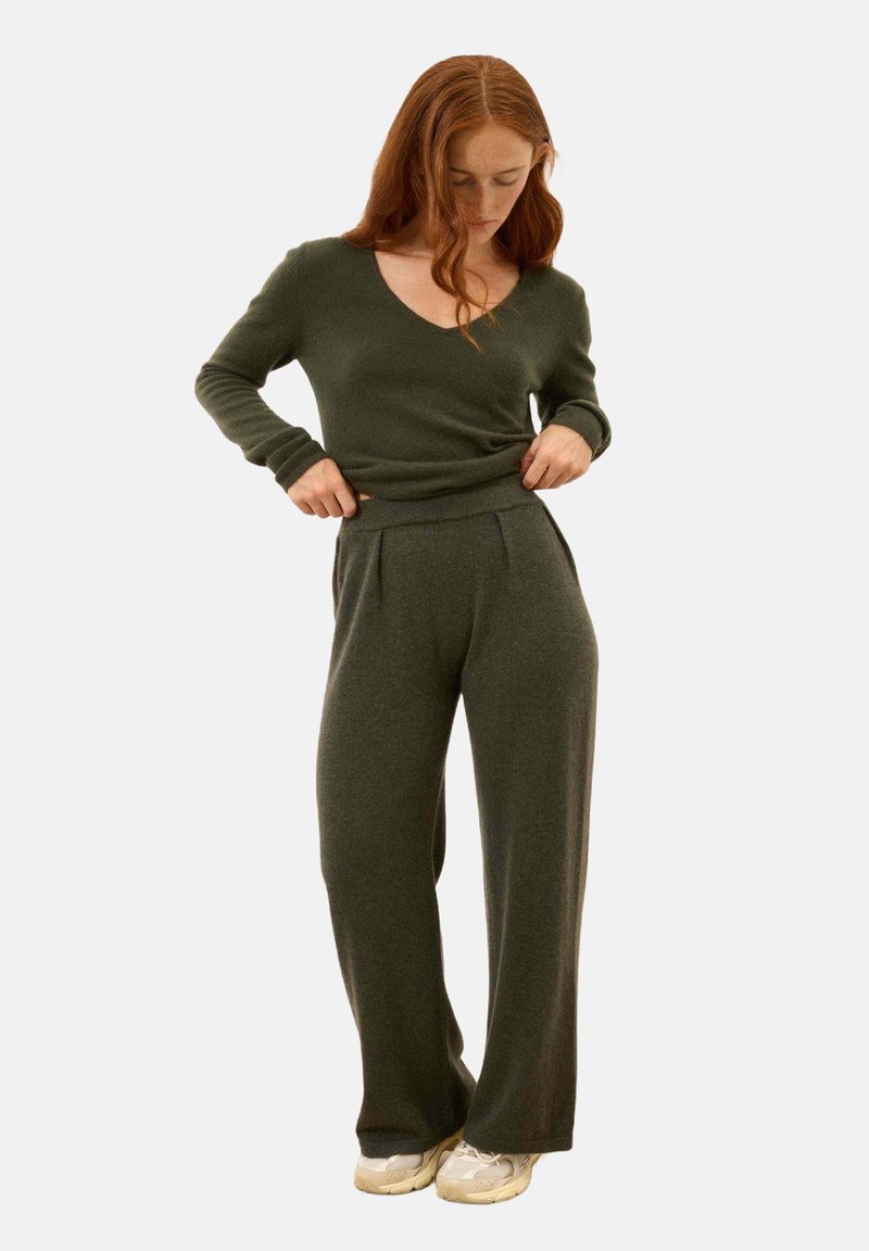 Zielony dzianinowy sweter z dekoltem w serek i długimi rękawami, w połączeniu z ciemnozielonymi spodniami typu wide-leg. Oba elementy mają miękką fakturę.