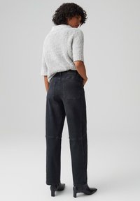 Jeans neri a vita alta con gamba dritta, dotati di tasche posteriori e cuciture sottili. Abbinati a un top corto a maniche corte in grigio chiaro con texture.