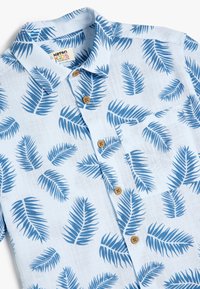 Camicia azzurro chiaro a maniche corte con un motivo di foglie di palma in blu scuro. Presenta un colletto, chiusura con bottoni e una tasca sul petto con bottoni marroni.