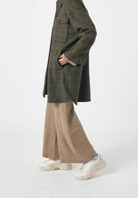 Grøn- og blåternet uldfrakke med to lommer, beige vide bukser og klumpede hvide sneakers. Tekstureret stof og oversized design.