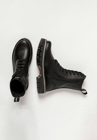 Bottes de combat en cuir noir avec un laçage à l'avant, bout rond, semelle robuste et fermeture éclair sur le côté. Tirette notable sur le talon.