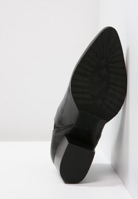 Musta nahkakenkä, jossa on teksturoitu kumipohja ja tyylikäs, teräväkärkinen muotoilu. Yksivärinen ilman näkyviä kuvioita tai koristeita.