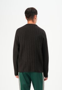 Maglione scuro a coste con maniche lunghe, design semplice, scollatura rotonda e texture morbida, abbinato a pantaloni da tuta verdi con strisce bianche.
