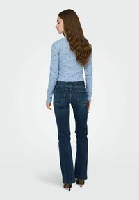 Haut bleu clair à manches longues avec de petits pois noirs, associé à un jean évasé bleu foncé. Le jean comporte deux poches arrière et un ourlet effiloché.