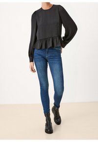 Top nero a maniche lunghe con finitura testurizzata e orlo arricciato, abbinato a jeans slim-fit blu e stivali neri alla caviglia.