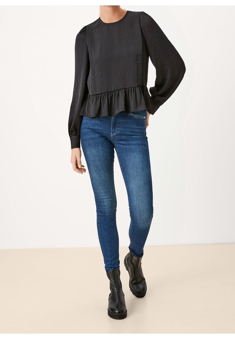 Top nero a maniche lunghe con finitura testurizzata e orlo arricciato, abbinato a jeans slim-fit blu e stivali neri alla caviglia.