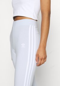 Lichtblauwe leggings met een hoge taille. Voorzien van drie witte zijsstripes en een klein wit Adidas-logo op de dij. Zachte, rekbare stof.