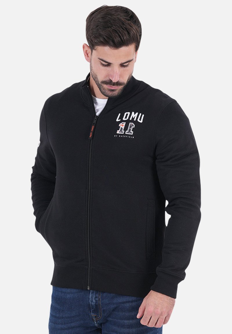 Sweatshirt zippé noir en tissu doux, avec un col haut, des poches latérales et un logo imprimé blanc sur la poitrine.