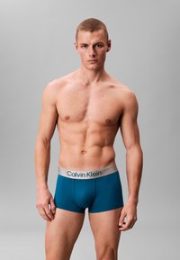 Męskie bokserki w kolorze morskim z miękkim, elastycznym szarym pasem z logo „Calvin Klein”. Gładka tkanina i dopasowany fason.