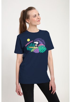 Kobieta w granatowej koszulce z Snoopym surfującym na desce wśród tropikalnych liści i napisem "Cowabunga!" różowym kolorem.