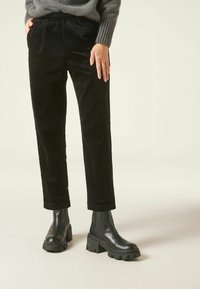 Pantalon en velours côtelé noir à coupe décontractée avec une taille élastique, associé à des bottines noires à semelle plateforme épaisse.