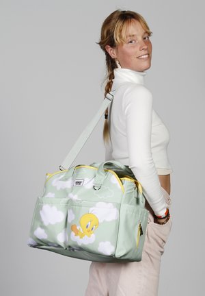 Bolso de tela verde con un diseño de pájaro de dibujos animados, que presenta acentos amarillos, patrones de nubes, dos asas en la parte superior y una correa de hombro desmontable.