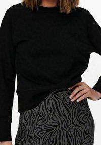 Sudadera negra con cuello redondo y mangas raglán, combinada con una falda gris que presenta un patrón de rayas de cebra negras.