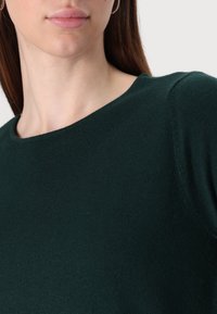 Σκούρο πράσινο πλεγμένο πουλόβερ με στρογγυλή λαιμόκοψη, που διαθέτει λεία υφή και καθαρό, απλό σχέδιο. Χωρίς ορατά μοτίβα ή διακοσμητικά στοιχεία.