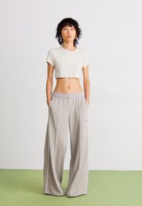 Pantalons larges gris clair avec des rayures blanches sur les côtés et une taille élastique, associés à un t-shirt blanc court. Finition textile lisse.