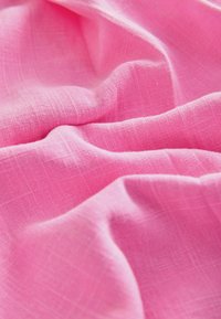Tissu rose pâle avec une texture de tissage visible, présenté avec des plis et des plis doux créant de la profondeur et des ombres.