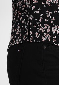 Svart topp med blommönster i pastellrosa och vitt. Slät tyg, figurnära design, med sidslits och diskret logotyp på svarta jeans.