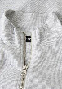 Pullover in tessuto grigio a coste con collo alto e zip argentata, dotato di un'etichetta nera all'interno con il nome del marchio.