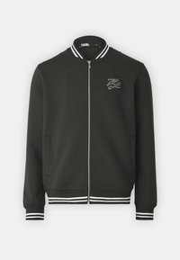 Tmavě zelená bomber bunda s plným zipem, bílými pruhovanými manžetami a lemem, s bílou vyšitou nášivkou na levé hrudi.