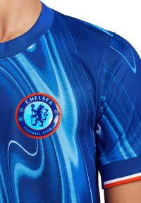 Sininen jalkapallopaita, jossa on kieppuva kuvio, pyöreä Chelsea FC -logo punaisena ja sinisenä sekä ohut kaulus oransseilla ja valkoisilla yksityiskohdilla.