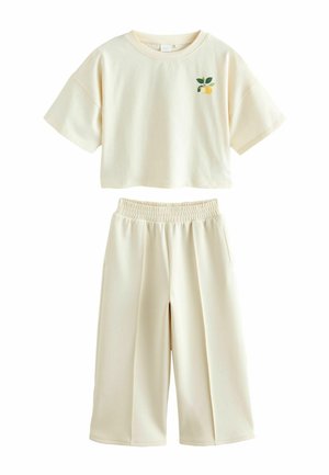 Cream-colored two-piece outfit with short-sleeve cropped top featuring a small lemon and leaf design, paired with wide-leg elastic waist pants.