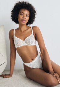 Set aus weißem Spitzen-BH und hochtaillierten Pants mit Blättermustern, transparenter Stoff und dekorativen Knöpfen. Weiches Material mit verstellbaren Trägern.
