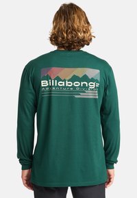 Zielona koszula z długim rękawem z wielokolorową grafiką gór oraz napisem "Billabong Adventure Division" na plecach. Materiał: bawełna.