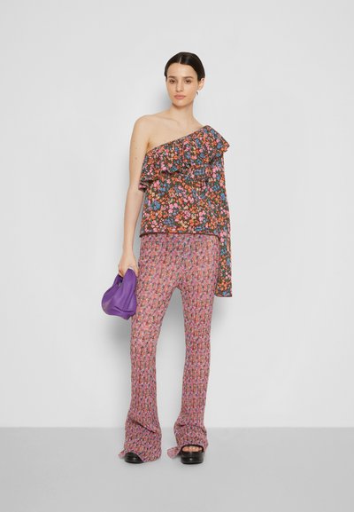 Top assimétrico com padrão floral e acabamento em babados, combinado com calças flare a condizer. Acessórios incluem uma bolsa roxa e sapatos de plataforma.